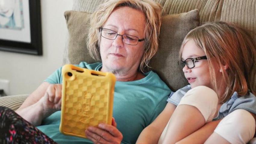 A woman and child look at the screen of a tablet