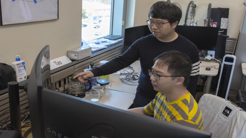 Assistant Professor Yalong Yang looks over the shoulder of Ph.D. student Tao Lu as they create a simulation of a news story presented in virtual reality.