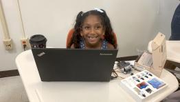A young student from USGI smiling while working at laptop computer