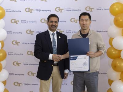 Two men shaking hands and standing in front of a step and repeat banner