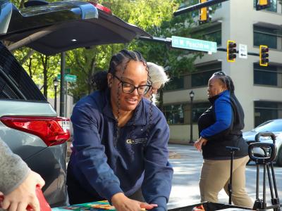 A smiling woman unloading food from a car. 