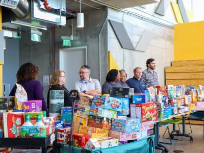 A group of people standing around a large amount of food for Klemis Kitchen. 